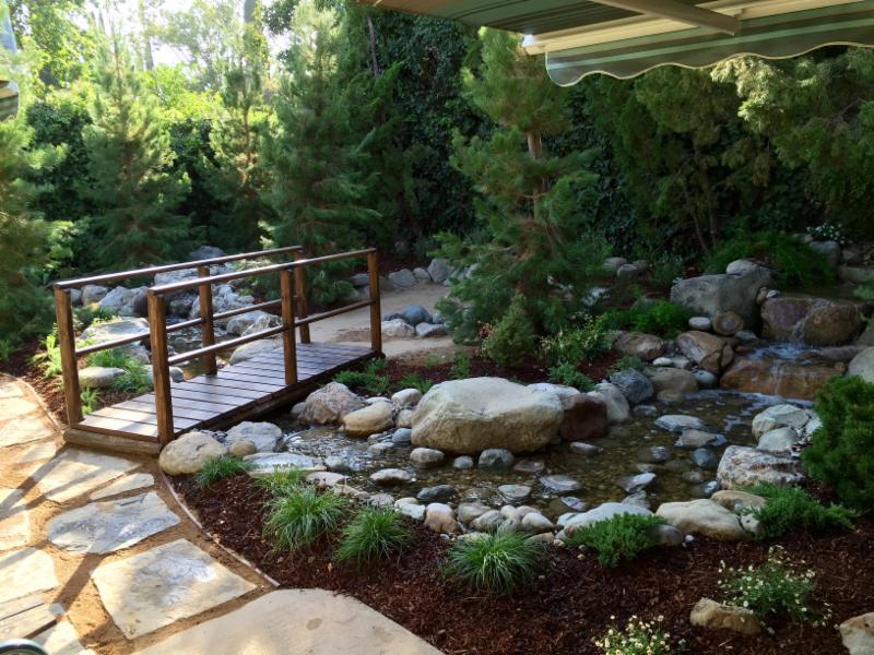 Natural pavers leading to a small birdge to wooded area. To  left is the pondless waterfall.